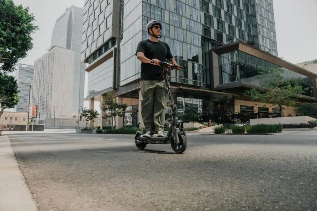 Segway MAX G3 Plus vs MAX G3: 12 More Real-World Miles and What Else Changed 2 Man riding an electric scooter on city street with modern glass buildings in the background.