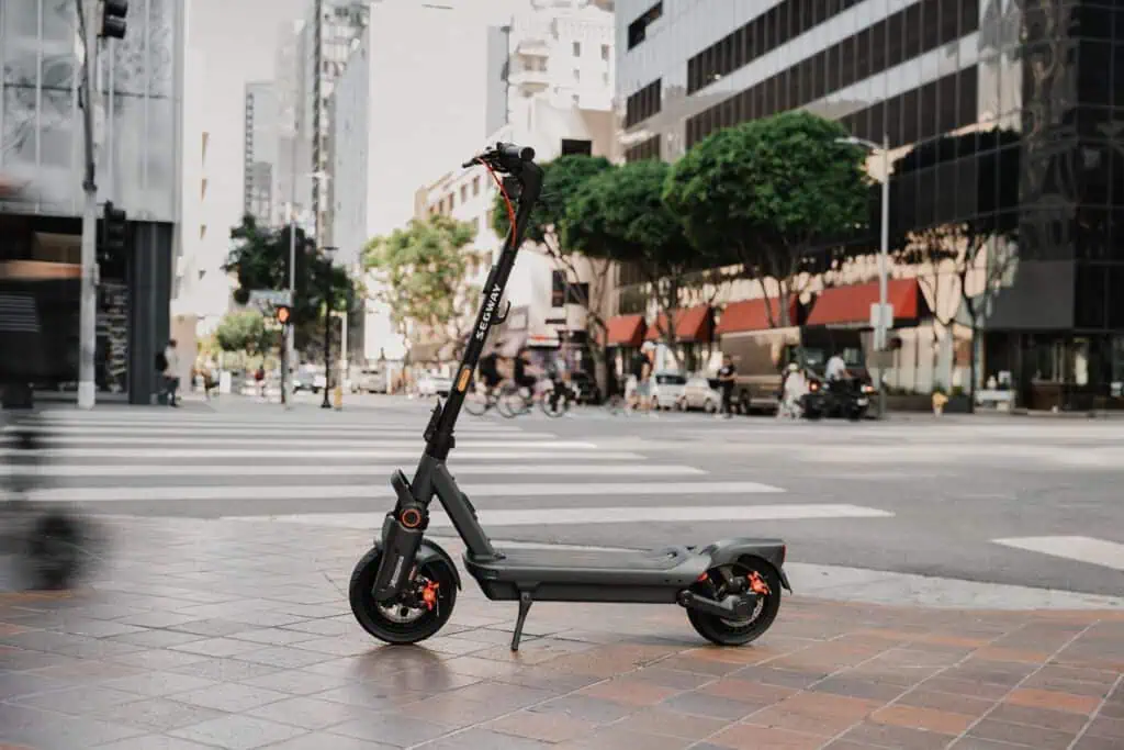 Electric scooter parked on city sidewalk with tall buildings and trees in the background.