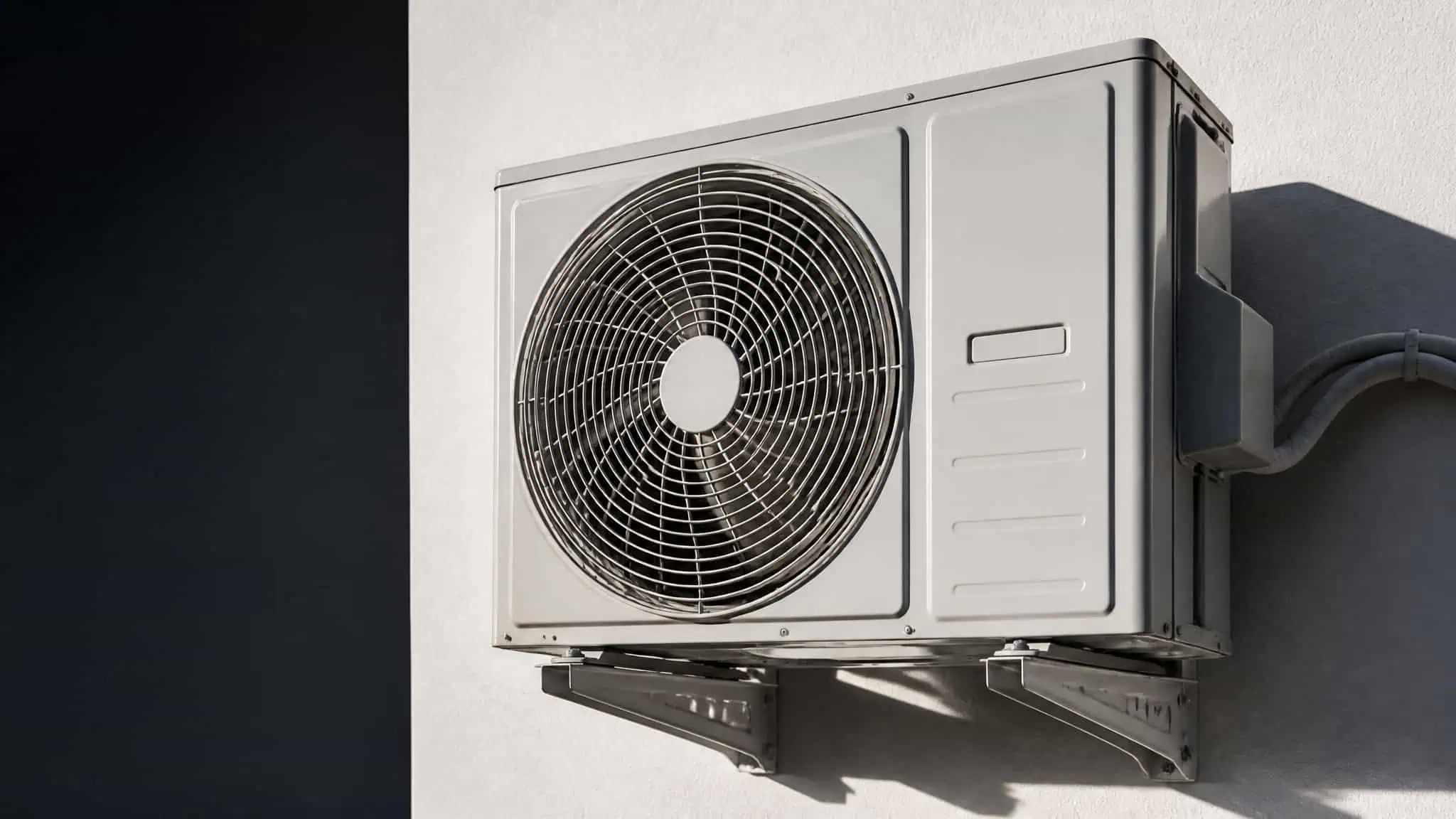 Modern outdoor air conditioning unit installed on a building exterior with a protective grille and mounting brackets.