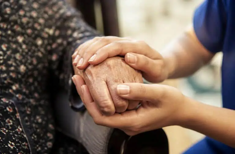 A caregiver gently holding an elderly person's hand, symbolizing compassion and support in senior care.