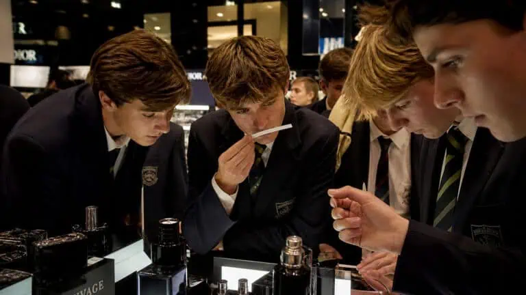 Group of young men in formal suits examining luxury perfume bottles at a high-end store, showcasing elegance and sophistication.