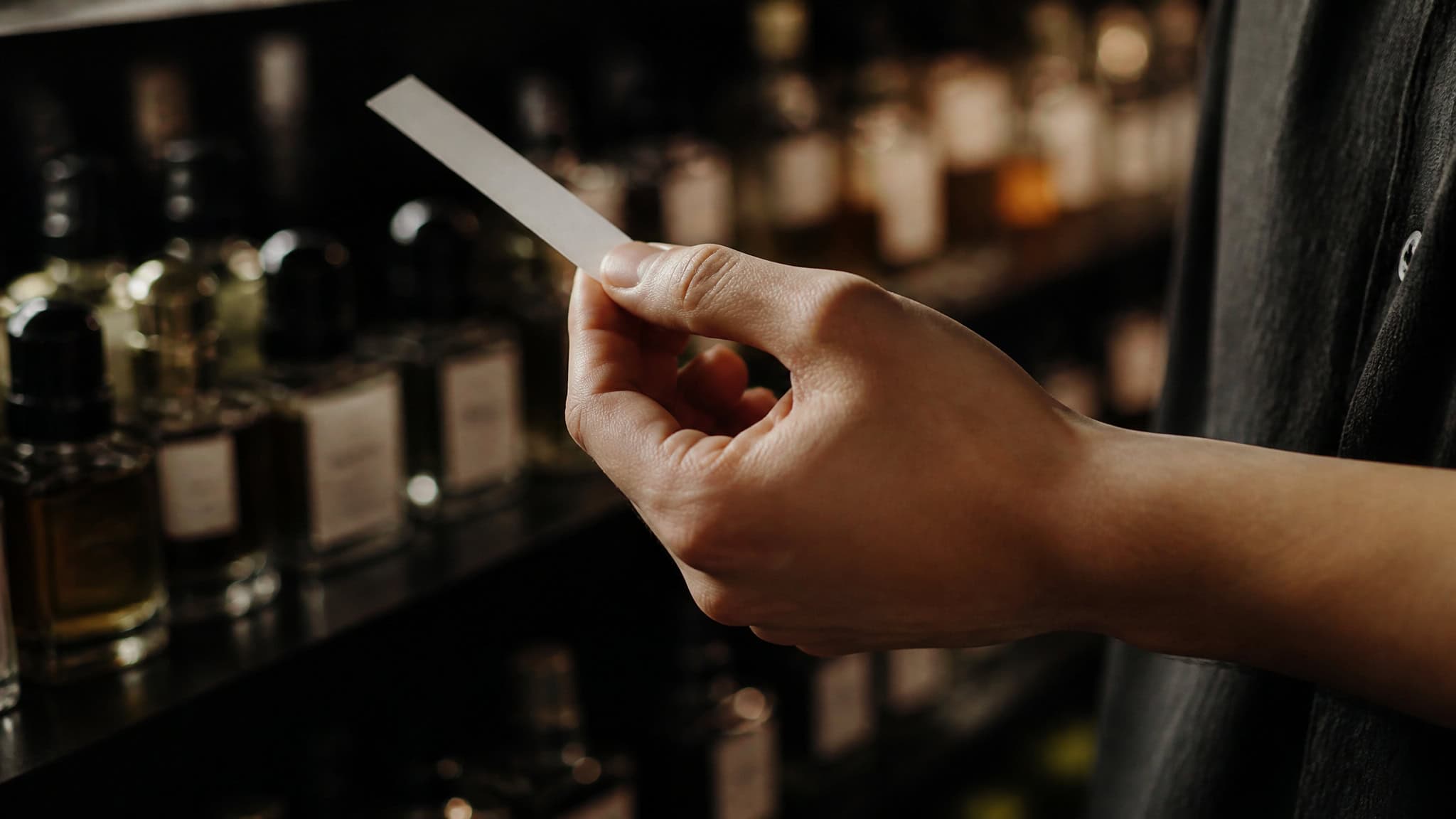 Perfume Obsessed Person: What Defines Them, Really 2 Hand holding a fragrance blotter card near perfume bottles