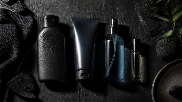 Collection of men's grooming products including shampoo, lotion, and cologne bottles on a dark textured surface with green leaves for a sleek, modern look.