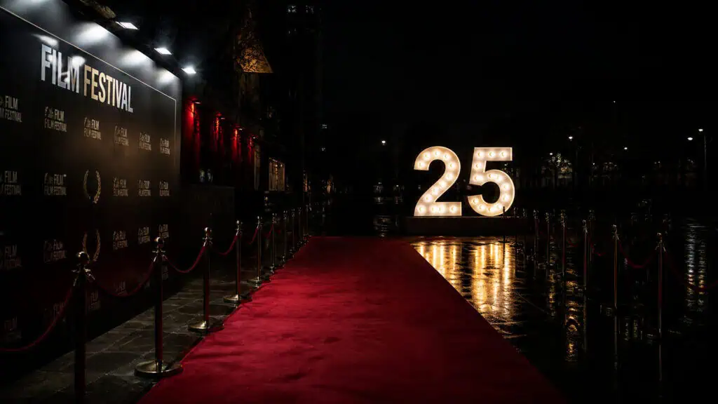 Red carpet leading to a large illuminated '25' sign at a film festival event during nighttime.