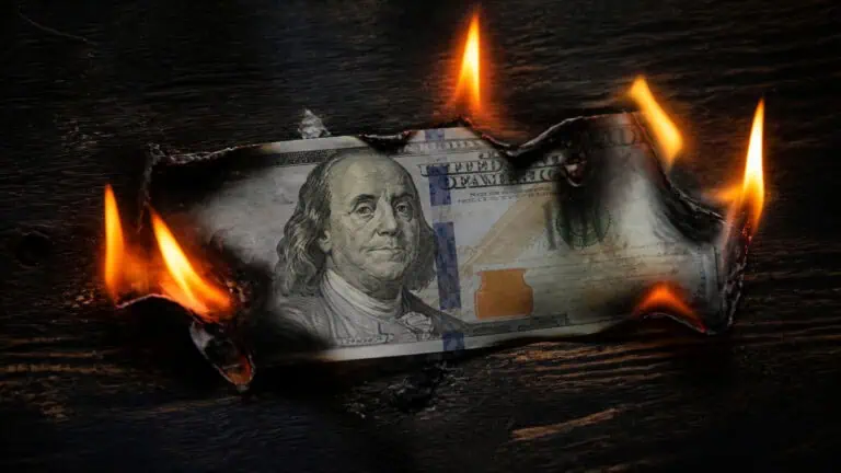 A $100 bill on fire with flames around it, symbolizing financial loss or economic crisis.