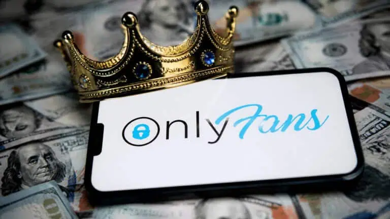 Smartphone displaying OnlyFans logo with a gold crown on top, surrounded by US dollar bills, symbolizing premium adult content and financial success.