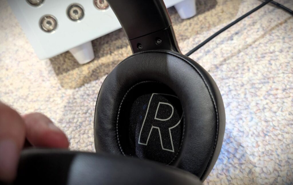 Edifier GX Professional Gaming Headset Review: Fortnite Nights With My Son Settled It 3 Edifier GX gaming headset earcup close-up with headband visible, black cushioning and stitched logo, on a textured surface.