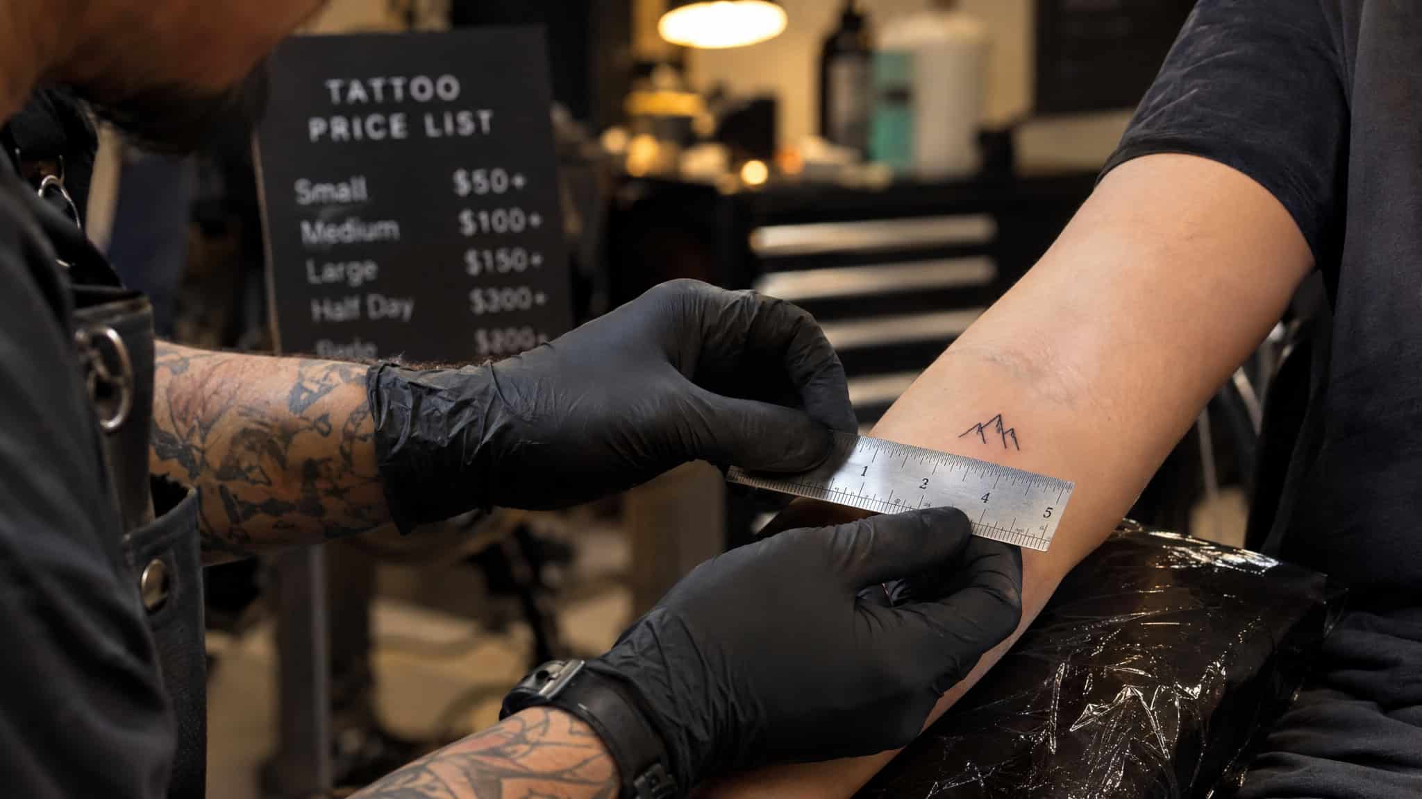 Simple Gaming Tattoo Ideas: 15+ Minimalist Designs, Credited Artist by Artist 5 Tattoo artist measuring a tiny gaming tattoo, illustrating shop minimums and small-tattoo pricing