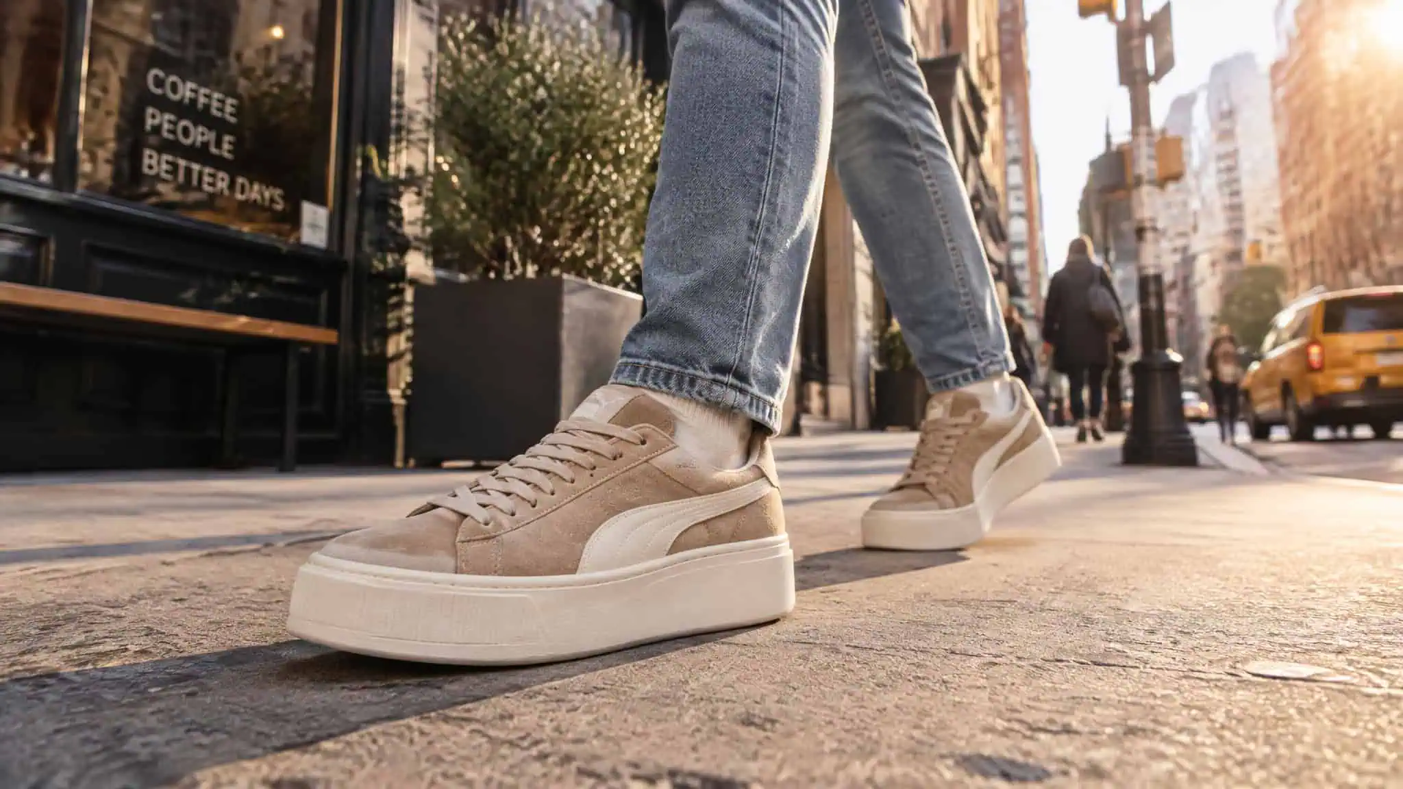 Shoes That Make You 2 Inches Taller: Lab-Measured Heel Stacks, Not Marketing Math 4 Close-up of beige casual sneakers worn by a person walking on a city sidewalk during sunset, with urban buildings and yellow taxi in the background.