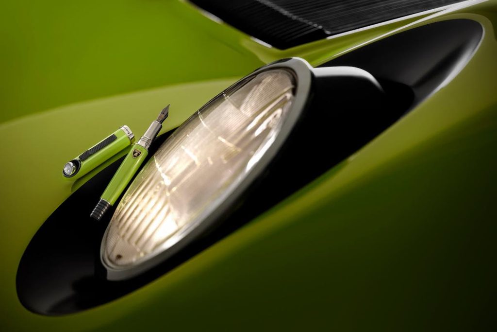 Close-up of a lime green Lamborghini Miura headlight with a matching pen resting on the car's body.