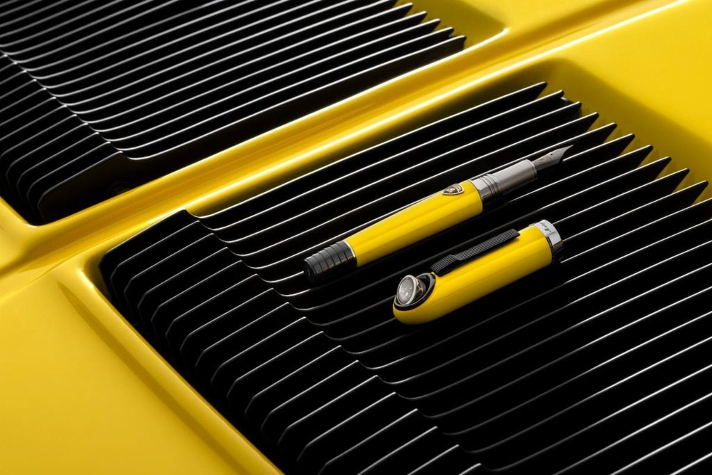 Close-up of a yellow Lamborghini Miura engine with black cooling fins and a yellow pen resting on it.