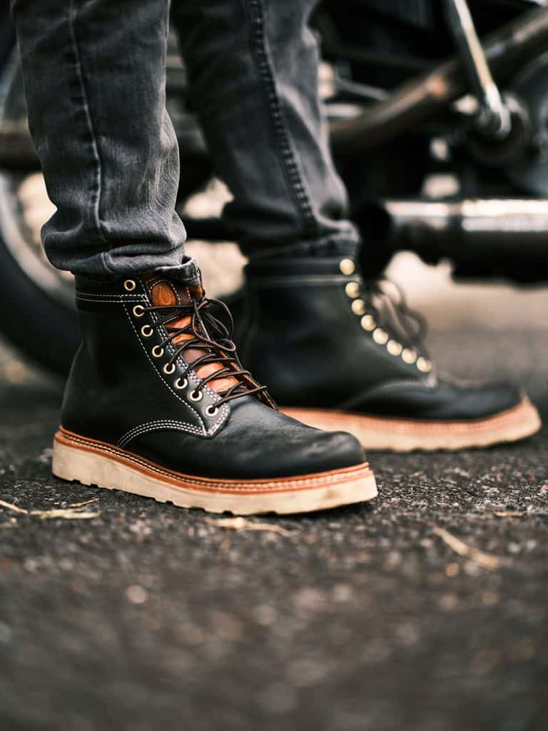 Close-up of black leather boots with tan soles worn with dark jeans, showcasing craftsmanship and style.