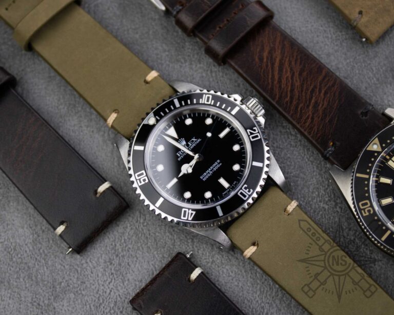 Luxury dive watch with a black dial and rotating bezel, paired with a green strap, surrounded by various watch straps on a gray surface.