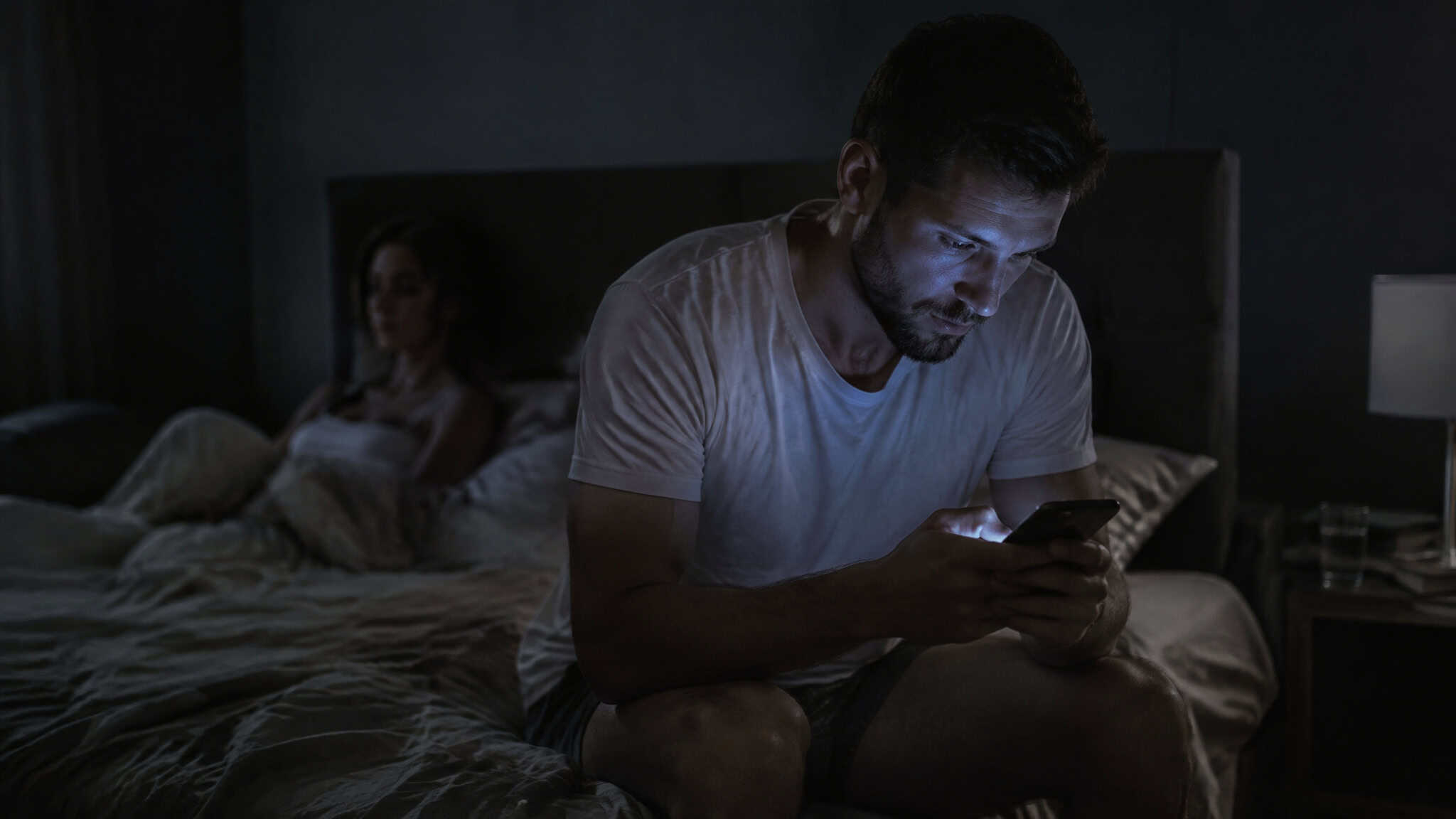 Man checking his phone while ignoring a woman after a hookup, showing post-sex emotional distance