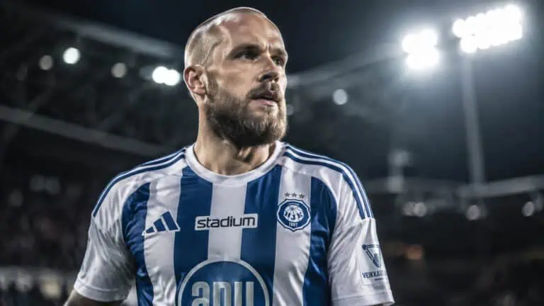 A male football player with a beard and short hair, wearing a blue and white striped jersey, on the field during a night game with stadium lights overhead.